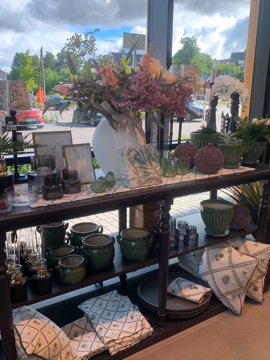 Krukker, planter og en vase med blomster på en hylle ved vinduet