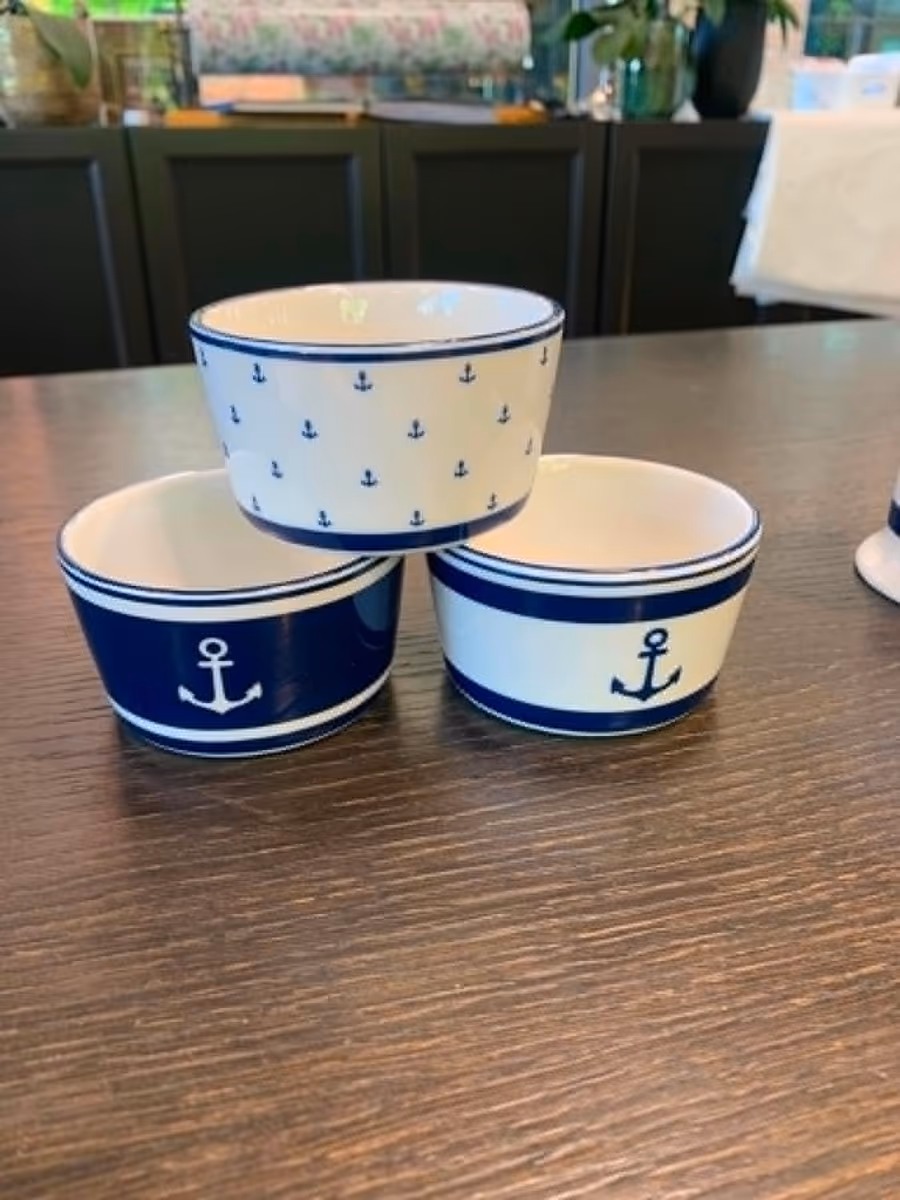 Skåler i hvitt porselen med marineblått ankermotiv, stablet på et trebord