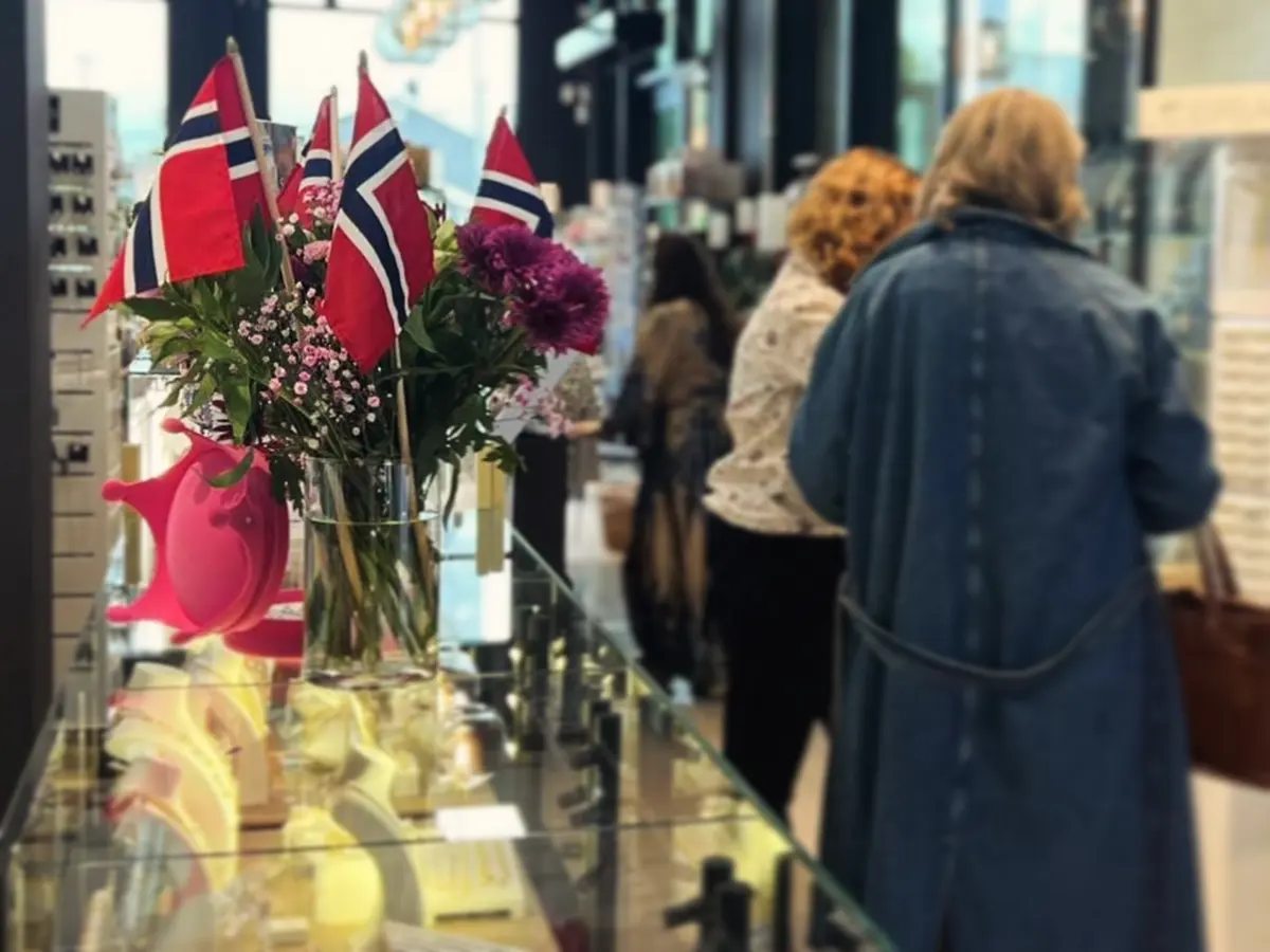 Kunder i kø langs monteren, med norske flagg og blomster i en vase i forgrunnen