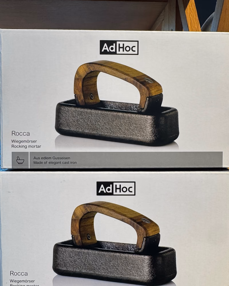 To stablede esker med AdHoc-morteren Rocca, med produktbilde og teksten «Wiegemörser / Rocking mortar» trykt på esken, hos Gressvik Gullsmed