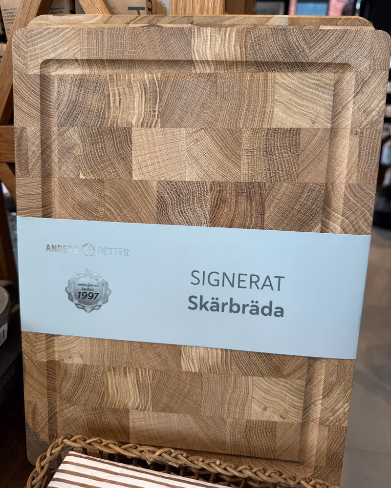 Skjærebrettet Signerat fra Anders Petter i endeved av eik, med banderole, stilt opp i hylla hos Gressvik Gullsmed