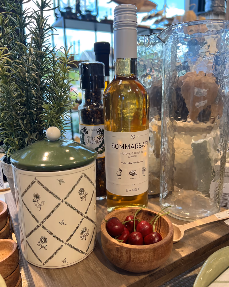 Flaske med Sommarsaft fra ERNST på en trefjøl i butikken, med kirsebær i en treskål ved siden av