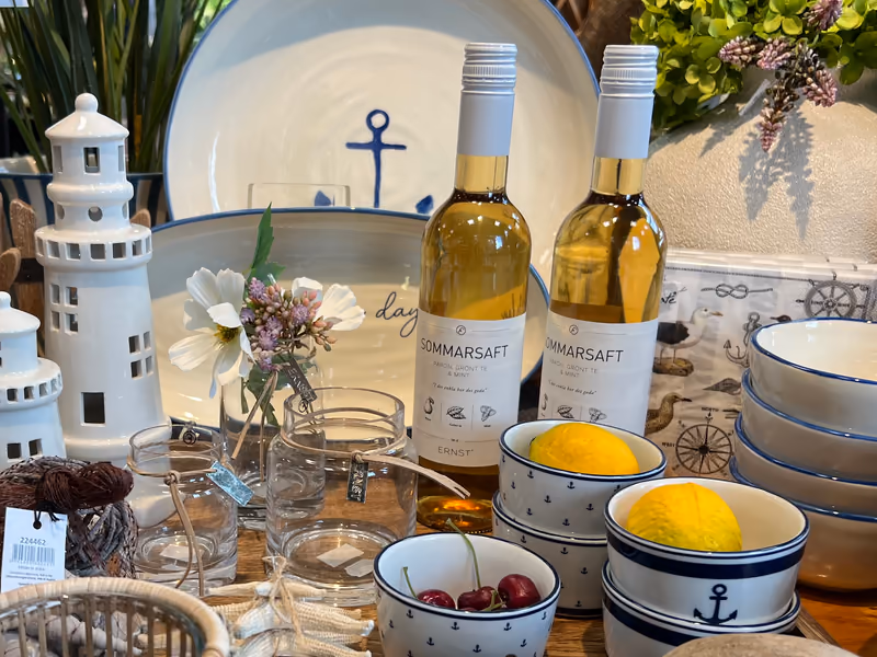 To flasker Sommarsaft fra ERNST i en oppdekning med skåler, sitroner og glass