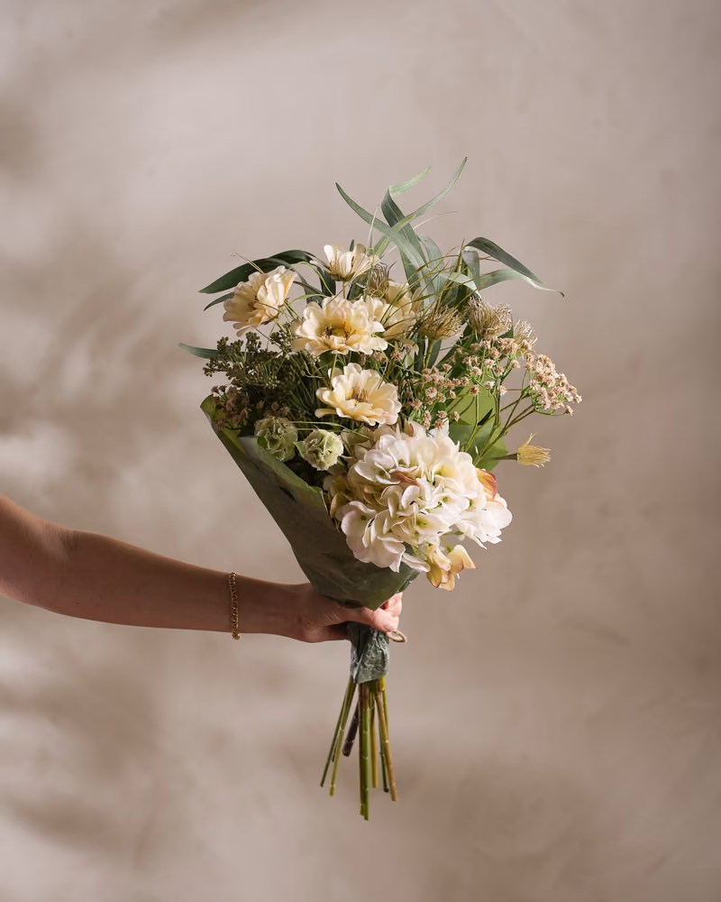 Hånd som holder en bukett kunstige blomster fra Mr Plant i hvitt og grønt