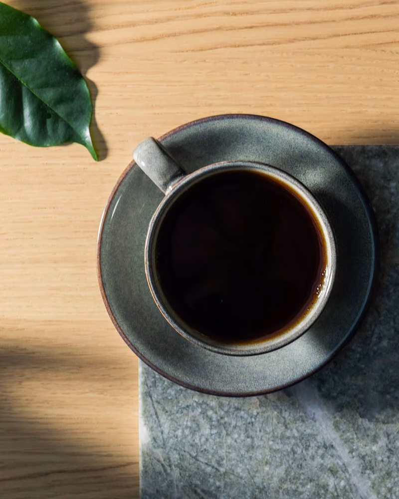 Kopp med svart kaffe fra Solberg & Hansen på en steinplate, med grønne blader ved siden av