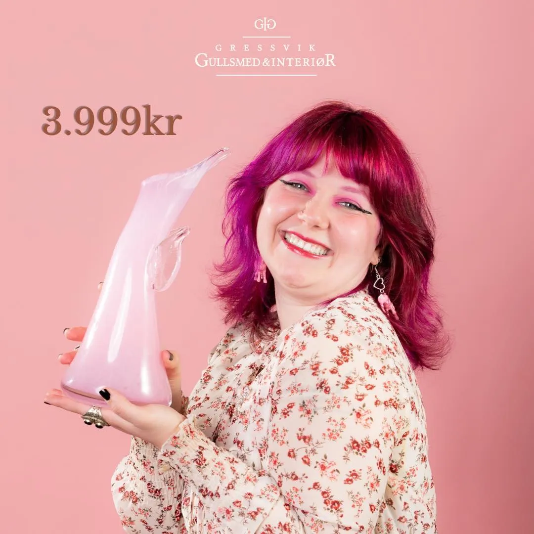 Maud Angelica Behn med rosa hår og blomstret kjole ler og holder Rosa sløyfe-vasen fra Magnor